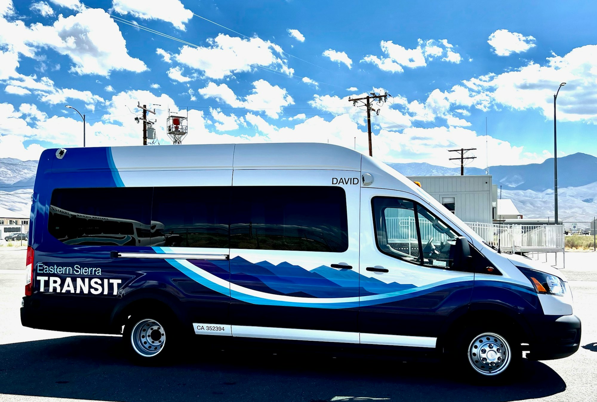A blue Eastern Sierra Transit van with mountain graphics parked outdoors under a clear sky.