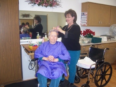 A woman in a wheelchair is getting her hair done by a hairstylist in a salon.