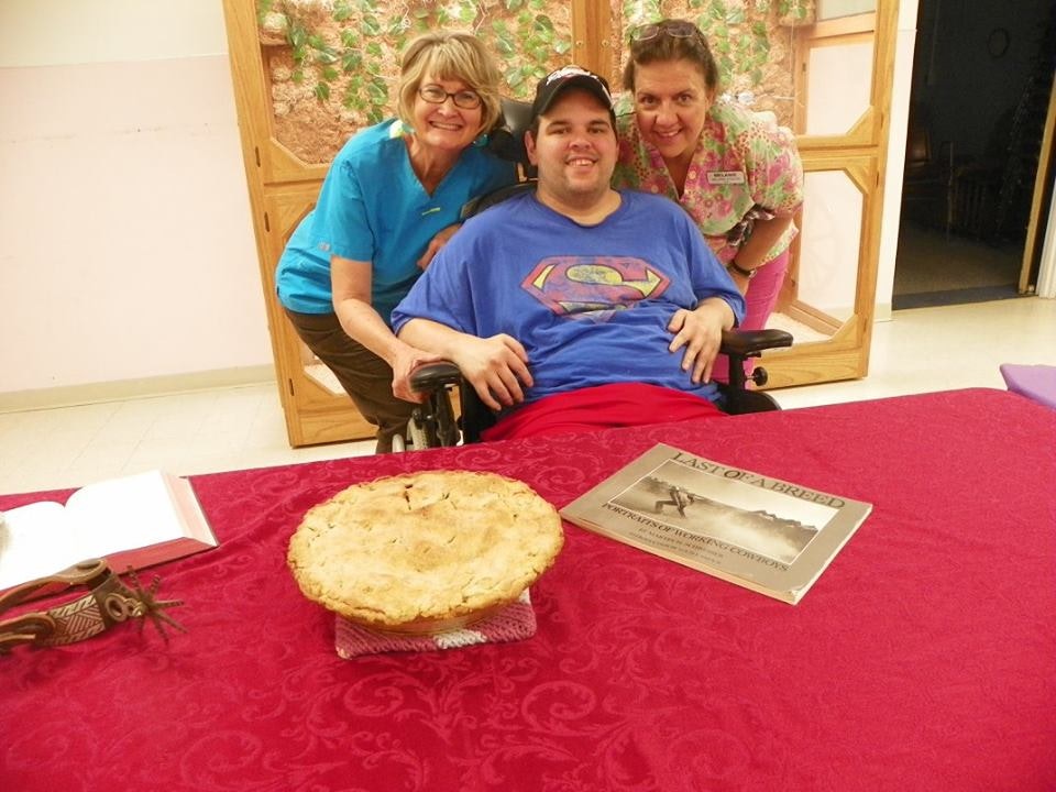 Three smiling people around a table with a pie and a book titled "Last of a Breed."
