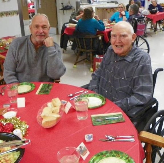 Two men smiling at a festive table with red tablecloth and holiday decorations around.