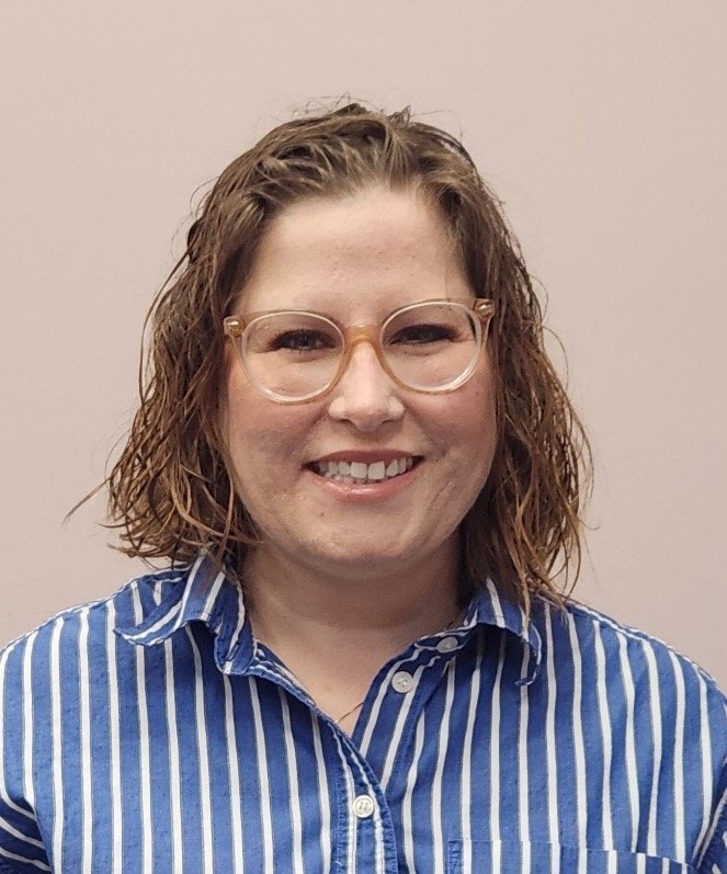 A person with glasses, wearing a blue and white striped shirt, smiles against a plain background.