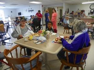 A busy indoor communal space with people eating at tables and staff walking in the background.