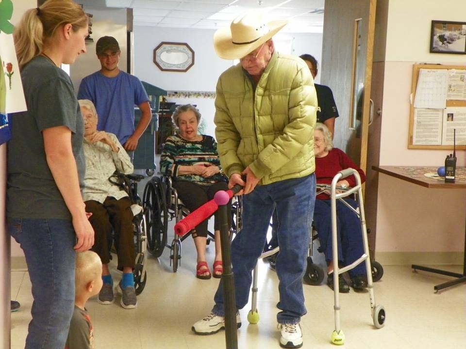 Elderly man with a walker, woman, child, and seated seniors in a hallway.