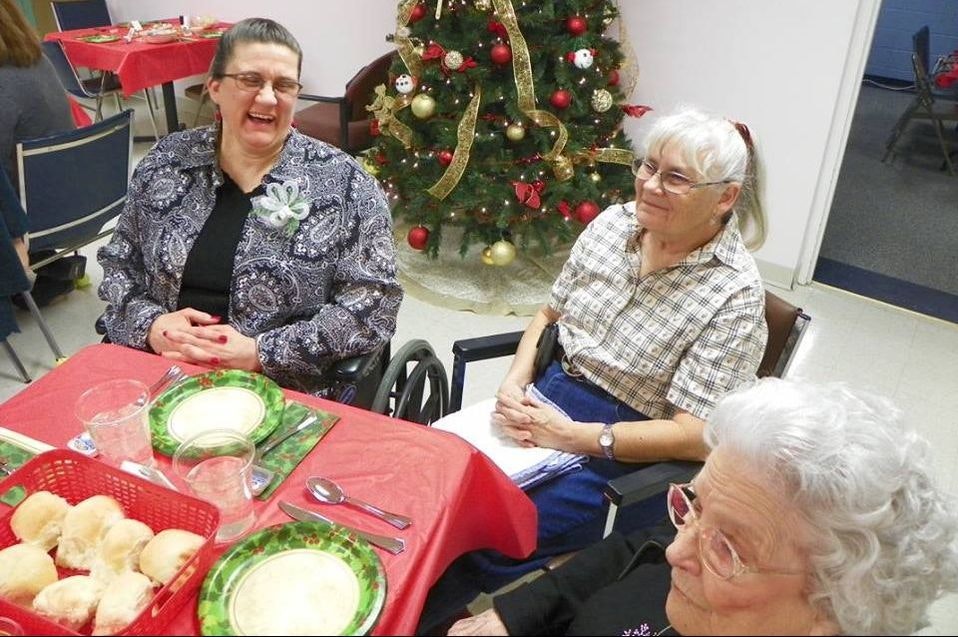 Three women at a table with festive decor and a Christmas tree in the background.