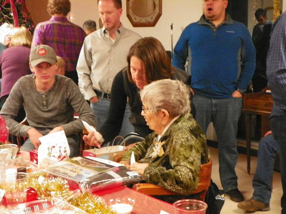 A group of people engaged in various activities at an indoor gathering, possibly a holiday event, with festive decorations on the table.