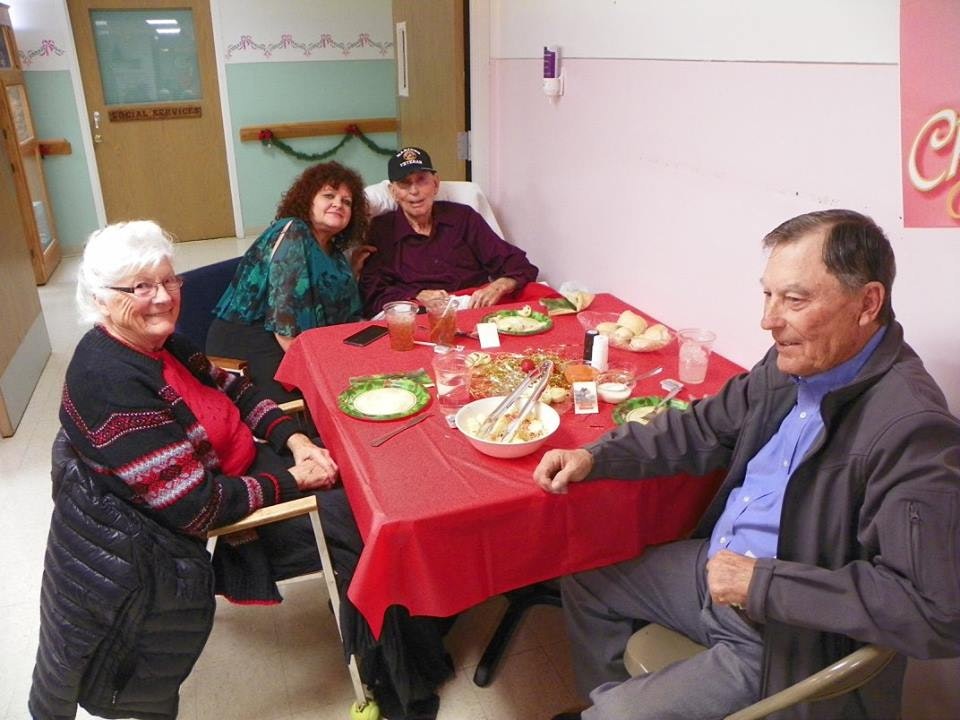 Four people at a table with food, smiling, in a room with holiday decorations.