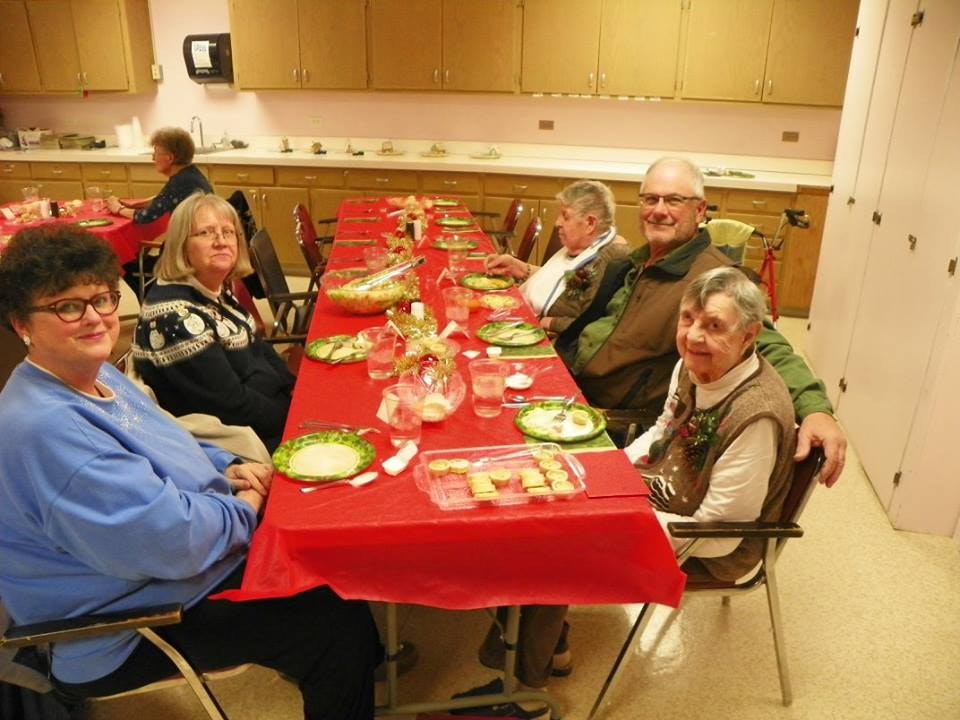 A group of elderly people sitting at a festively decorated table with a red tablecloth, enjoying a communal gathering.