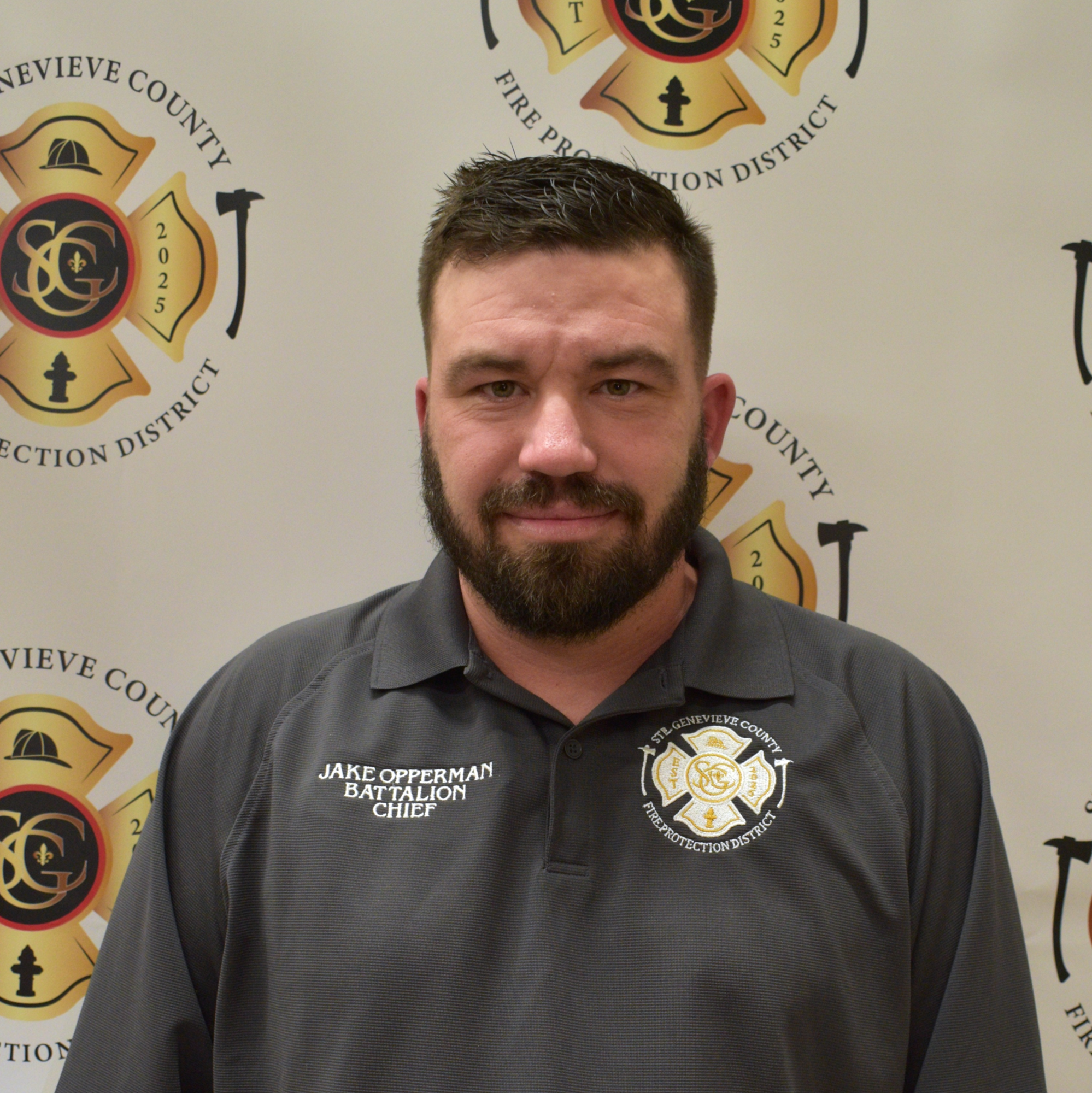 The image features a man with a beard wearing a gray shirt, standing in front of a fire protection district backdrop.