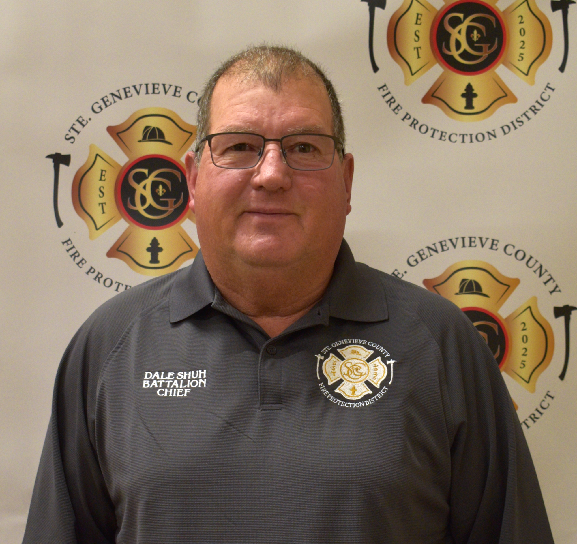A person in a gray shirt is identified as a battalion chief from the Ste. Genevieve County Fire Protection District, with a logo in the background.