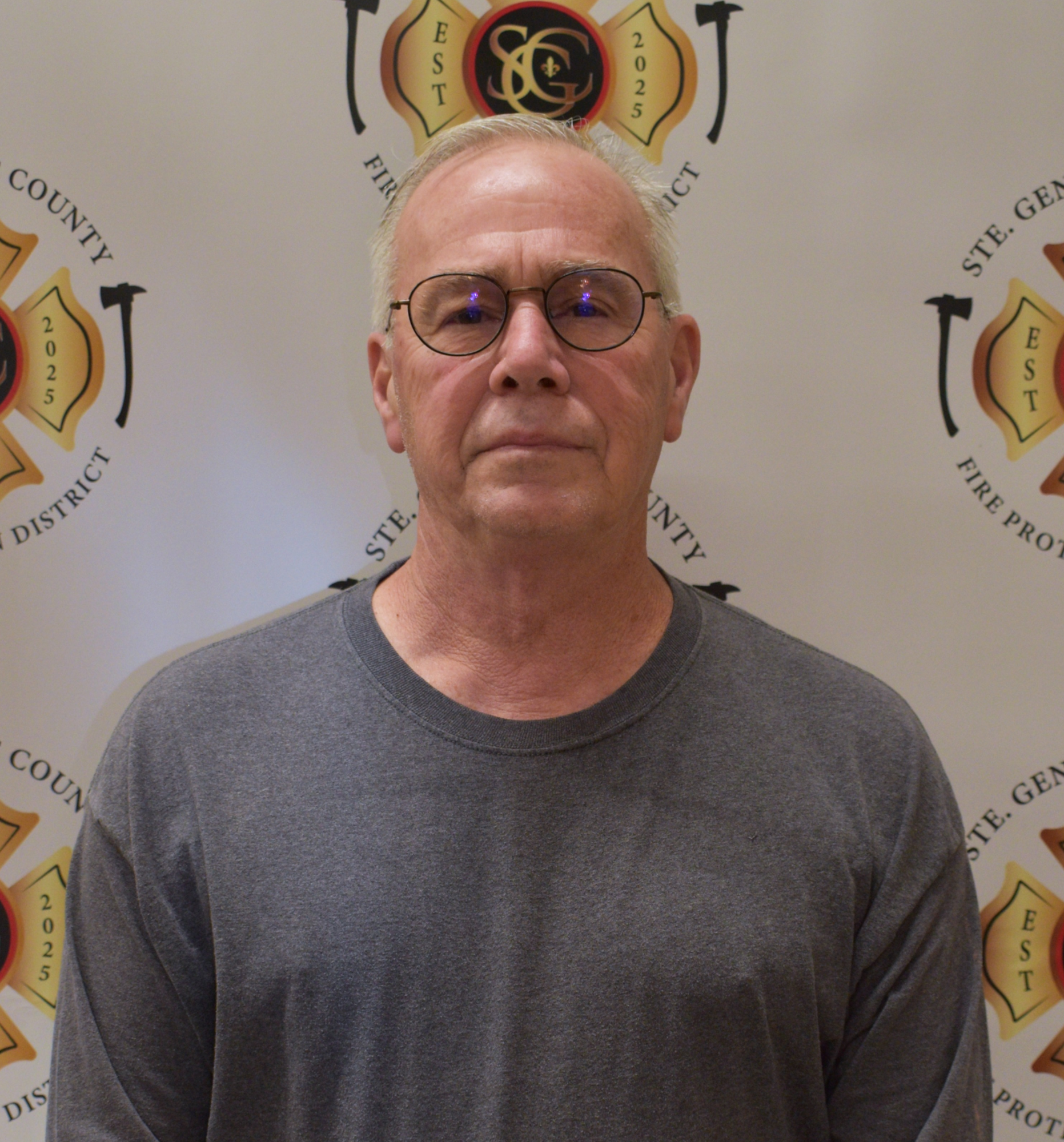 The image features a man in eyeglasses wearing a gray shirt, standing in front of a backdrop with a fire district logo.
