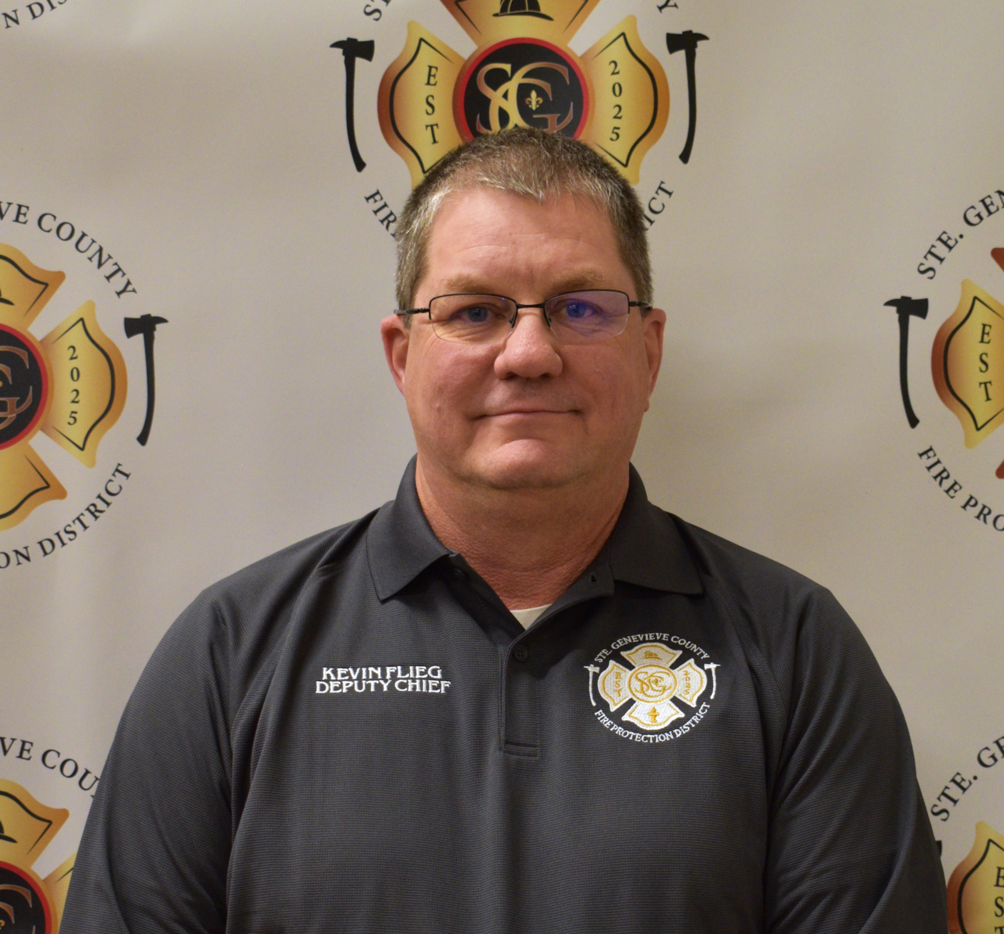 A man in a uniform shirt poses for a photo, with a fire protection district backdrop. Text includes "Deputy Chief" and his name.