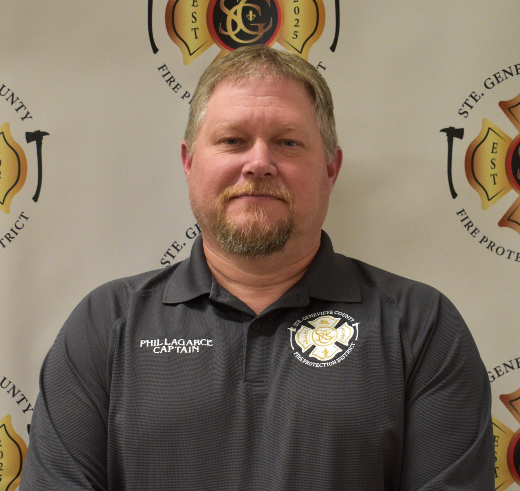 The image features a man in a dark shirt with a fire department emblem, posed in front of a fire protection district backdrop.