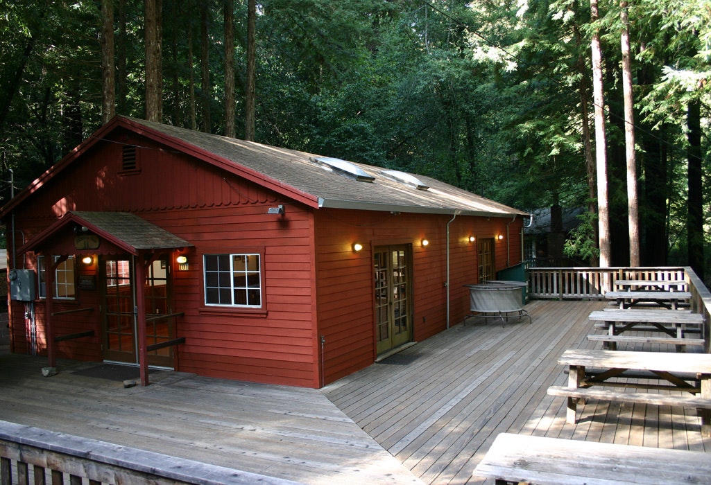 A red cabin with a deck surrounded by tall trees.