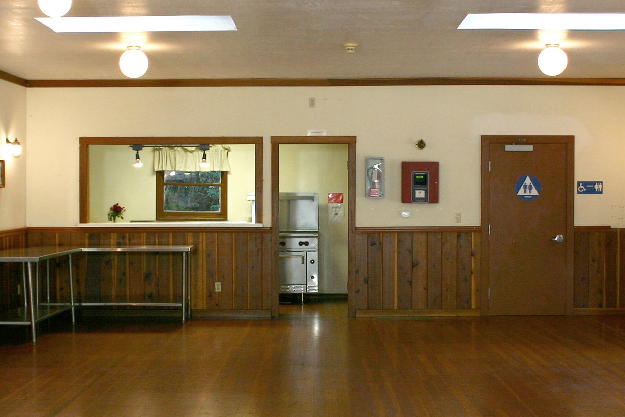 Interior view: empty room with wooden walls, two doors, service window, and ceiling lights.