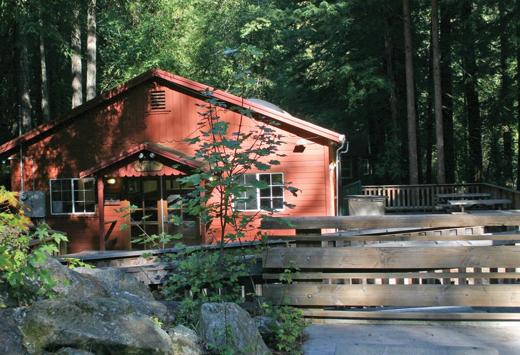 Red cabin with a porch in a forest setting.