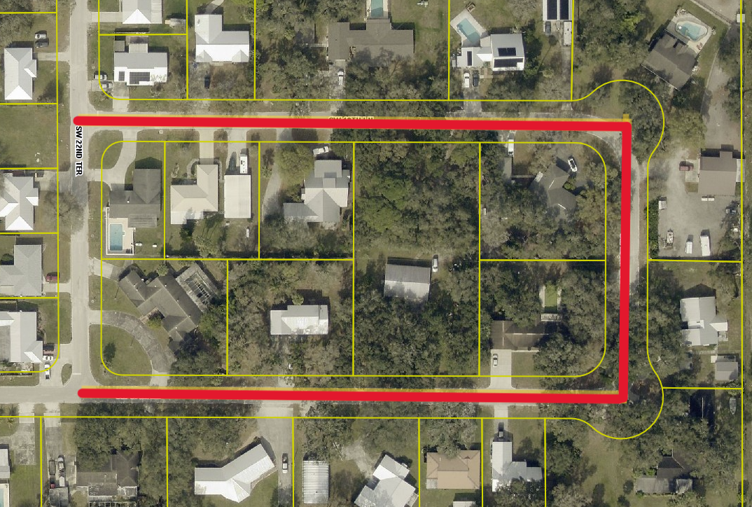 The image shows an aerial view of a residential neighborhood with houses outlined in yellow and a highlighted red road.