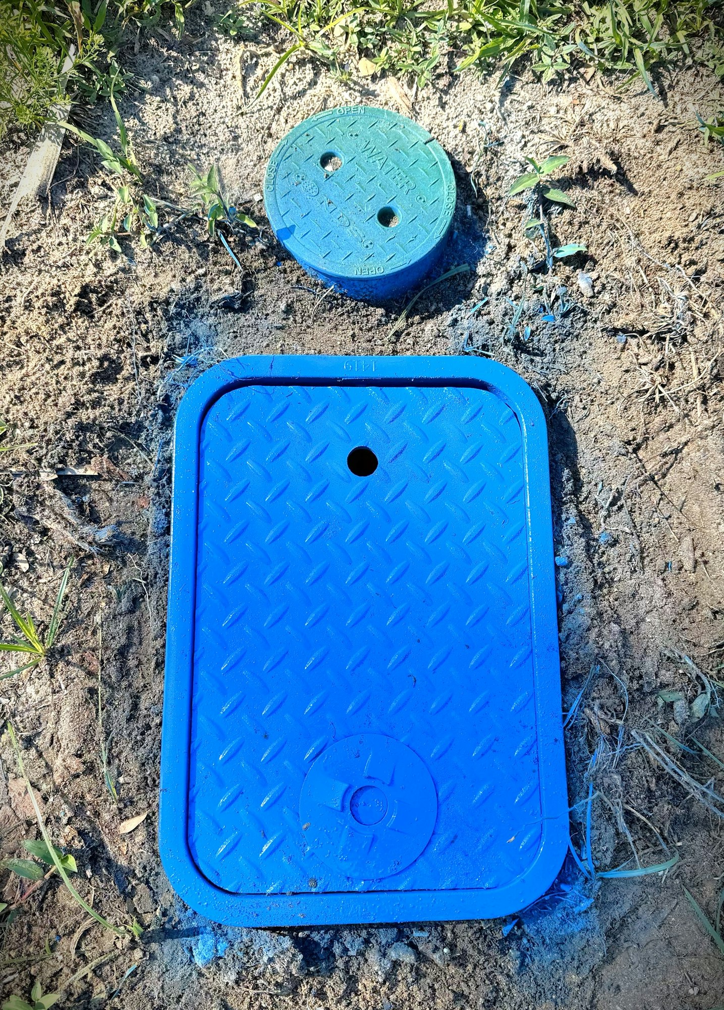 Blue and green water utility valve covers in dirt.