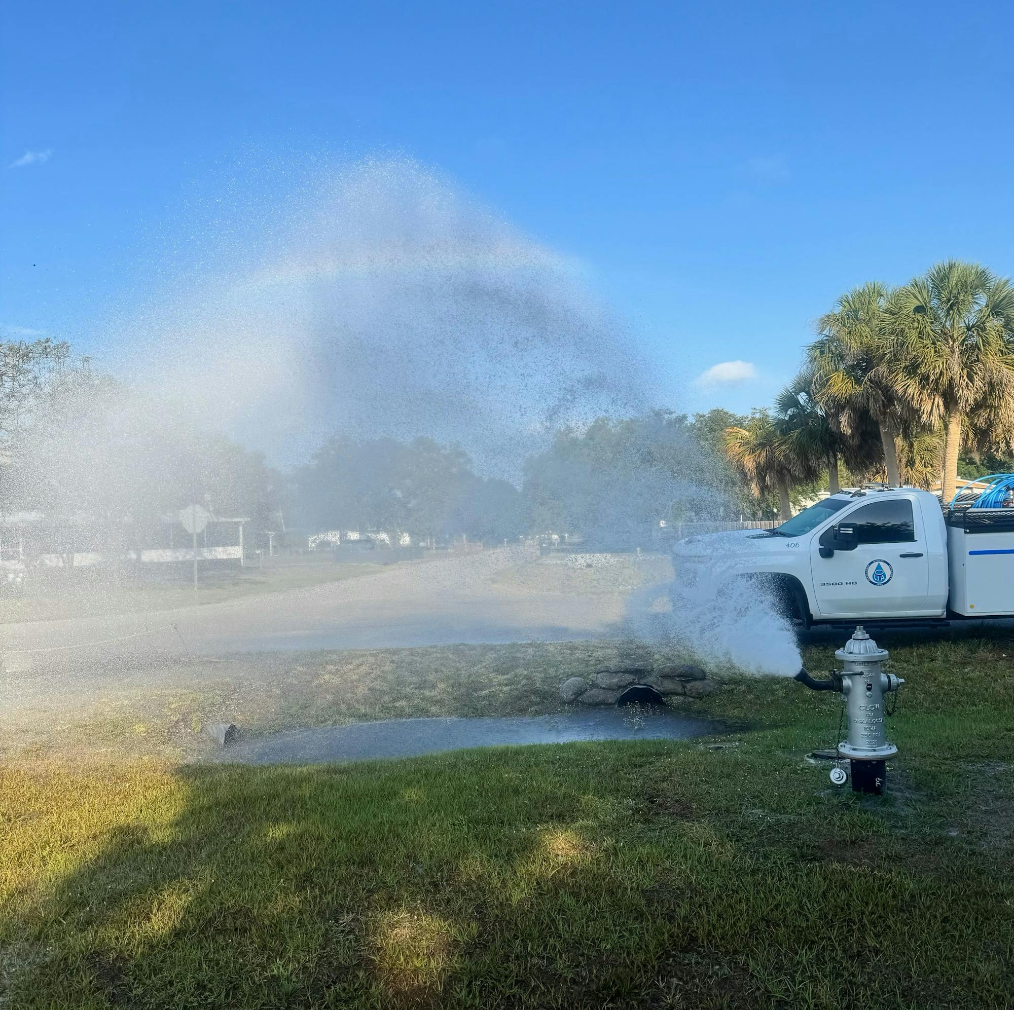A fire hydrant spraying water, creating a misty rainbow next to a parked utility truck.