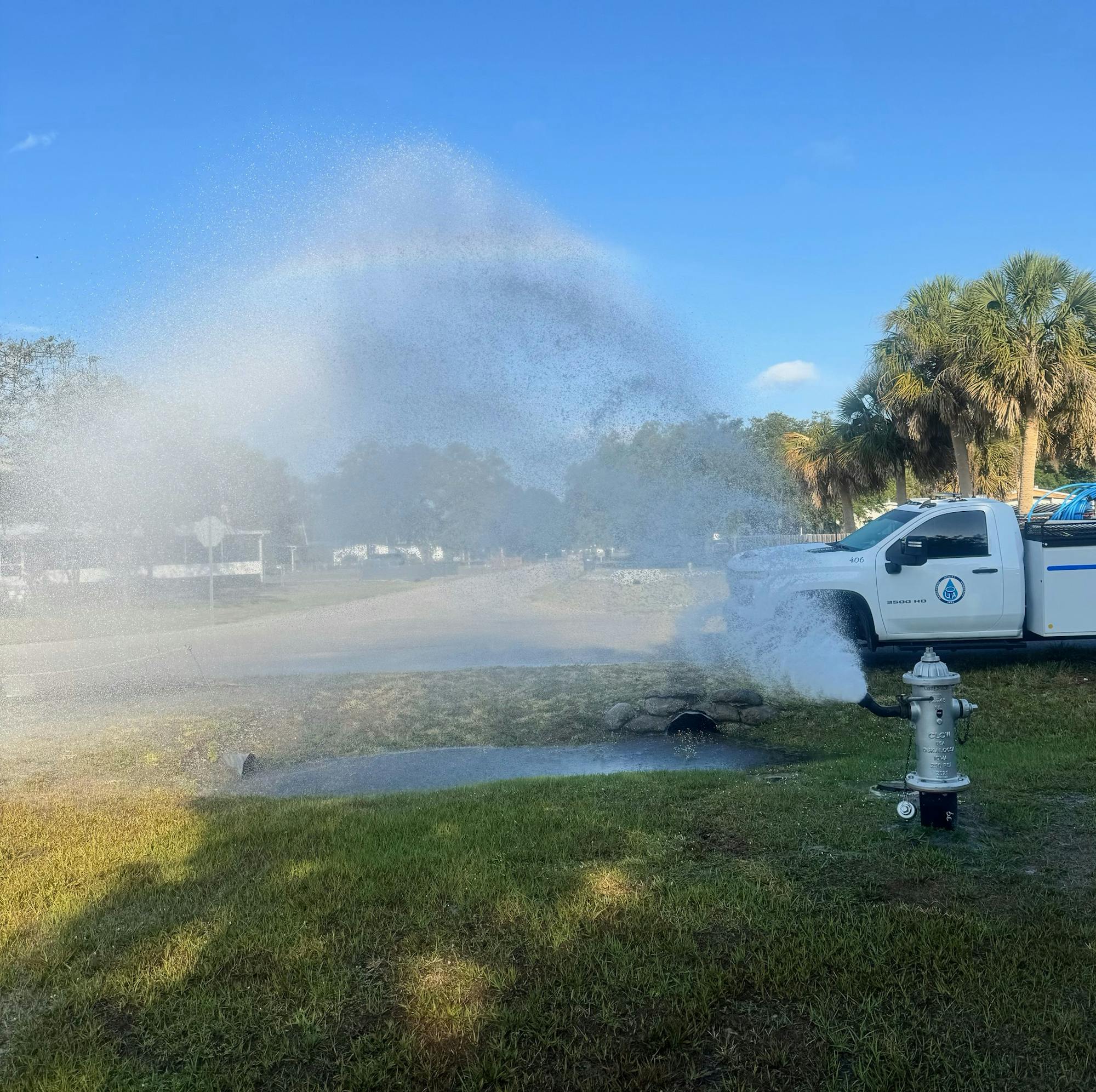 A fire hydrant spraying water, creating a misty rainbow next to a parked utility truck.