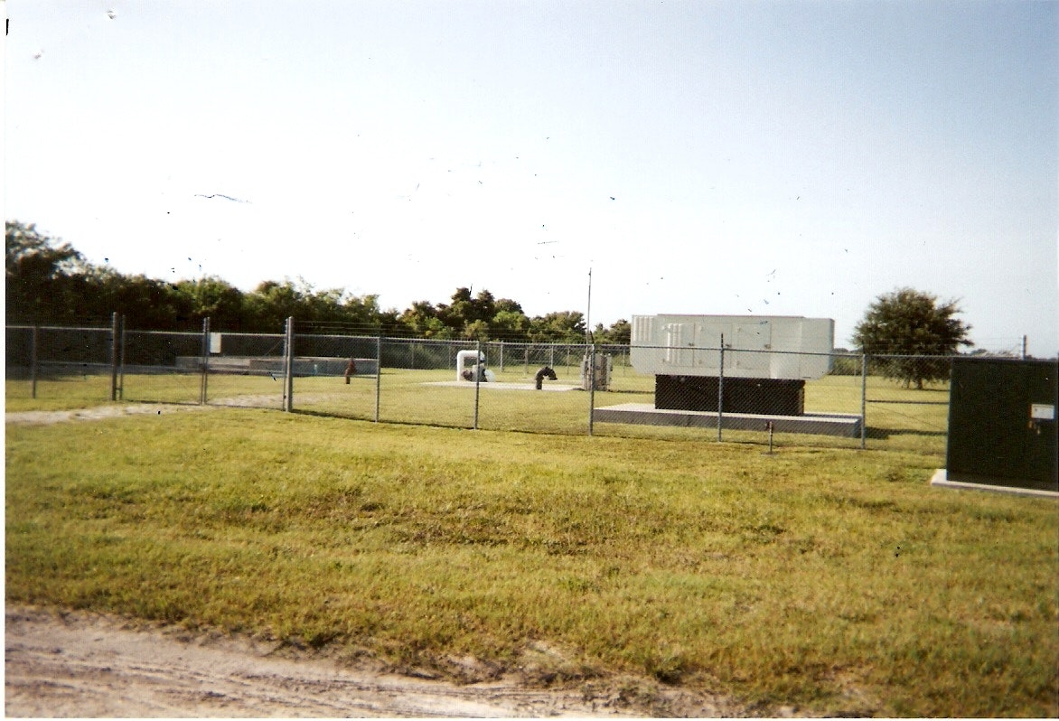 Fenced area with electrical equipment and a generator in a grassy field.