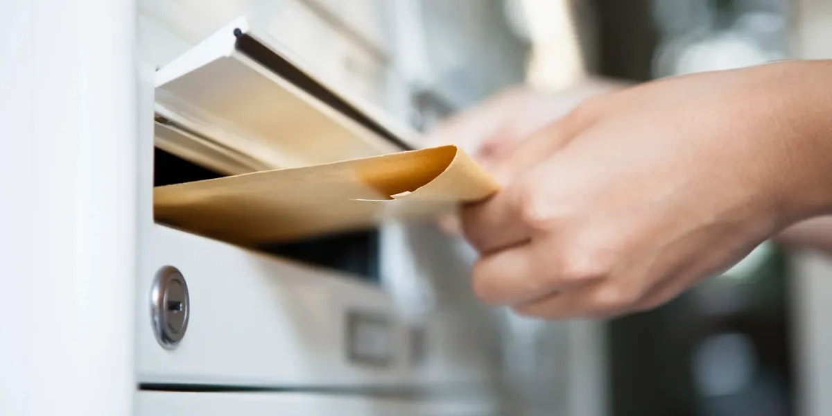 A hand is placing an envelope into a mailbox.