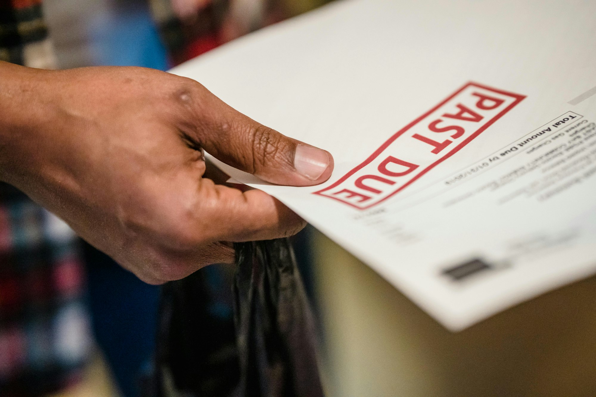 A hand holding an envelope marked "PAST DUE" in red.